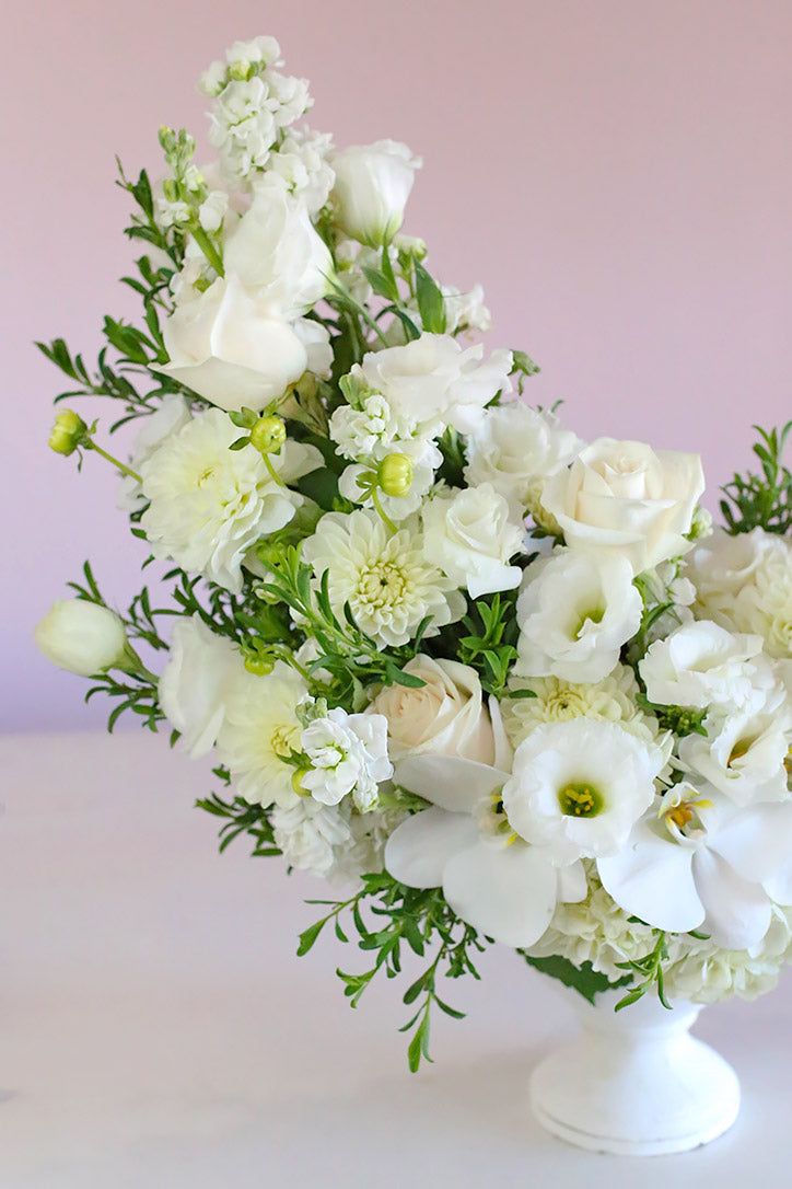 Side view of white roses, orchids, lisianthus and dahlias arranged in a chic white vase