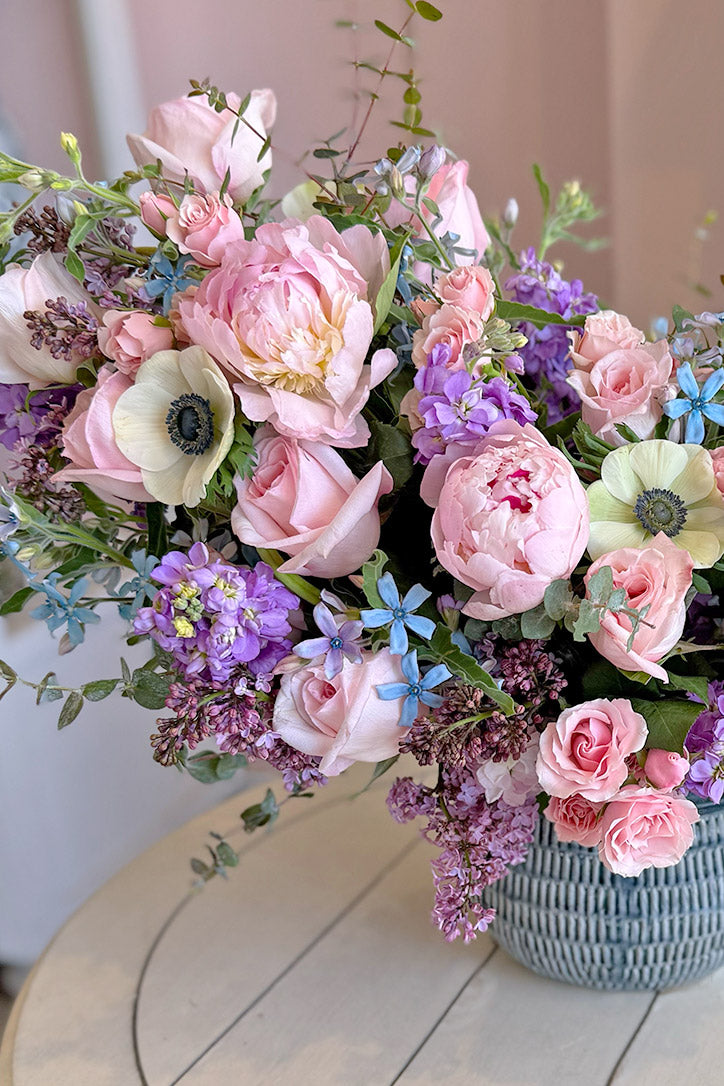Side view of the whimsical pink and purple arrangement in a glazed blue ceramic vase