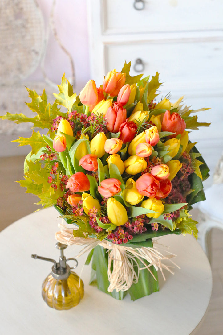 Yellow and orange tulip bouquet with pink waxflower in emerald paper