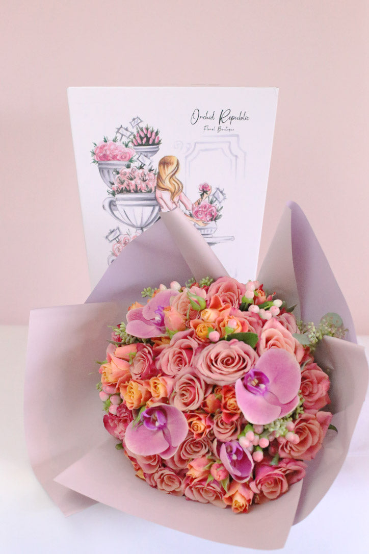Pink orchids above peach and blush roses with orange spray roses