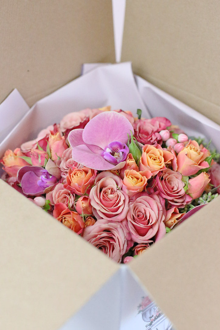 Close-up of bright pink Phalaenopsis orchids, peach roses and orange spray roses