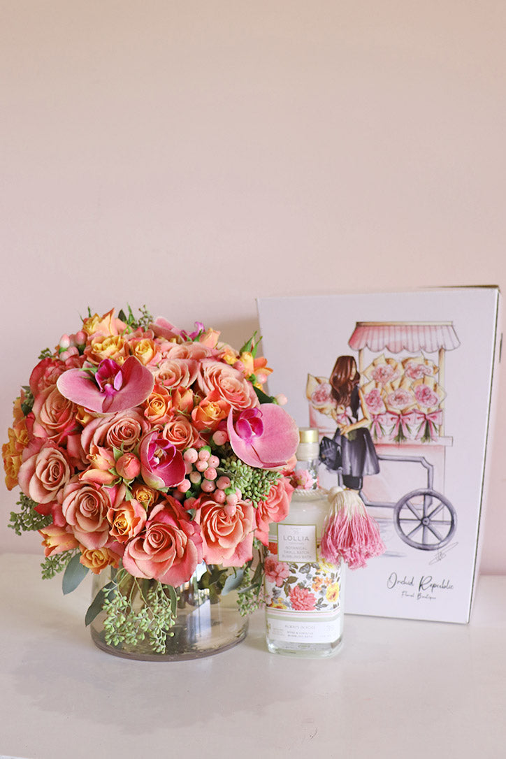 Pink orchids above peach and blush roses with orange spray roses