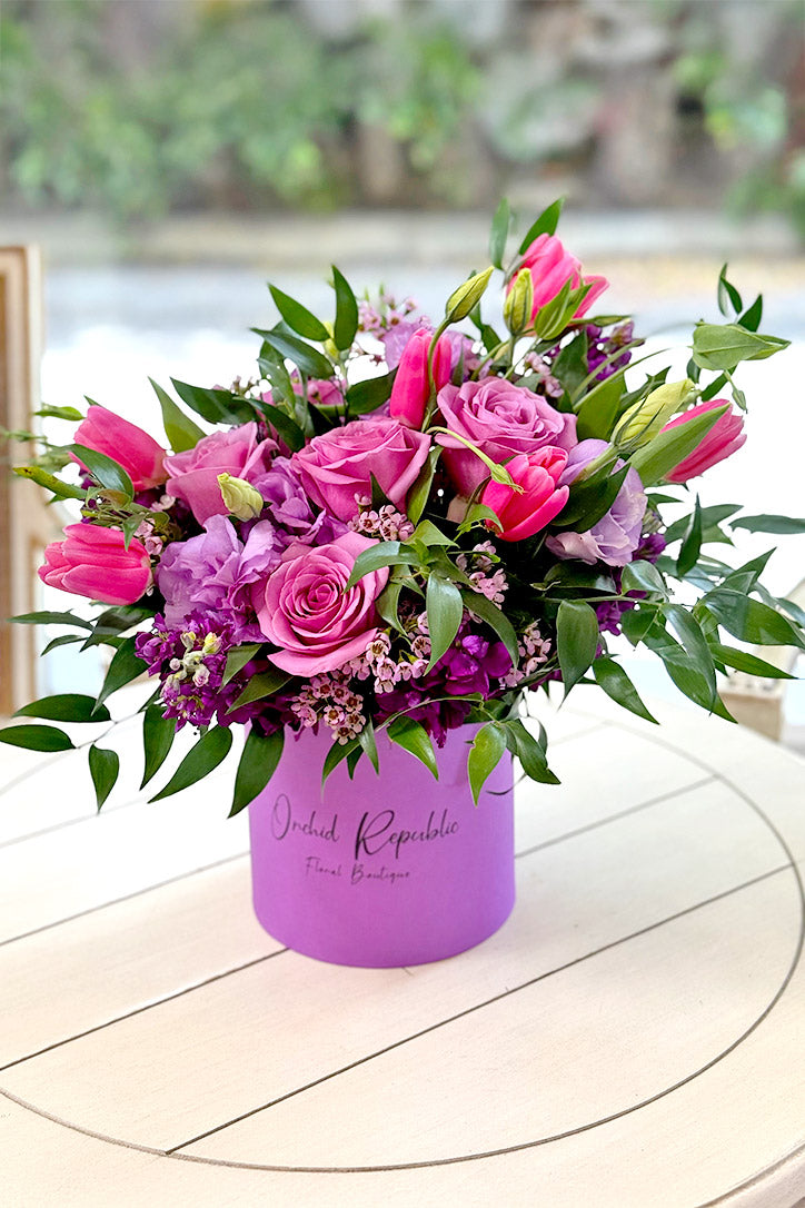 Mauve roses, hot-pink tulips and lavender lisianthus in a violet-green hat box