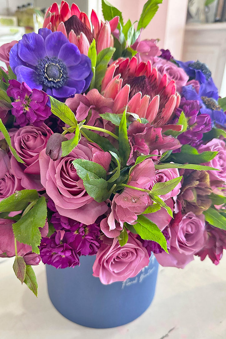 Side close-up of deep mauve and purple roses, proteas, hellebores, and anemones.