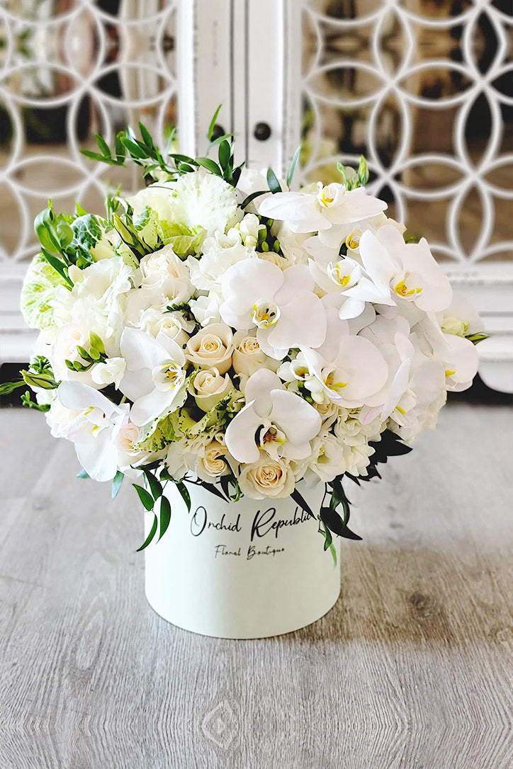 Elegant white orchids, roses and lisianthus arranged in a stylish white hat box