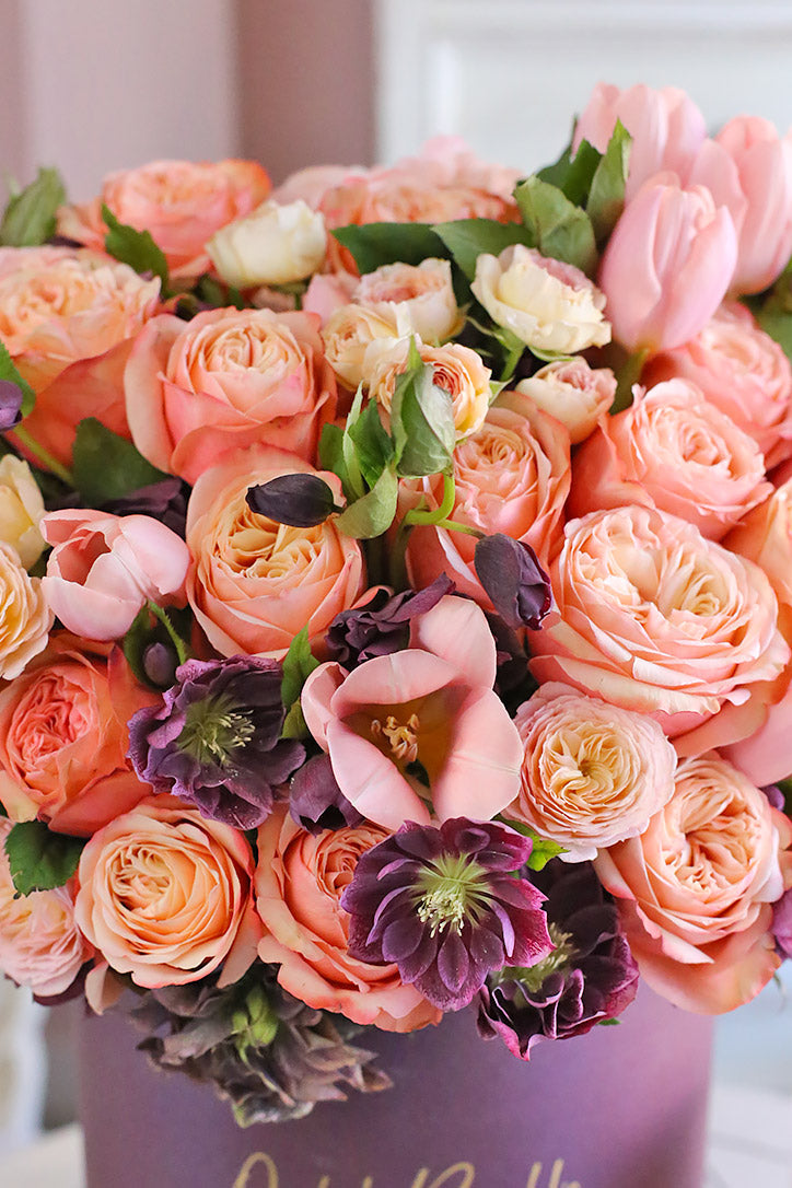 Close-up of velvety peach and pink roses with pastel tulips and delicate purple clematis