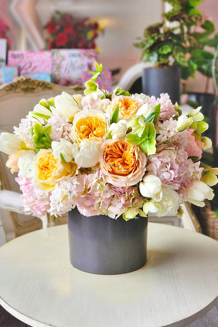 Peach garden roses, white tulips and green hellebores in a black vase