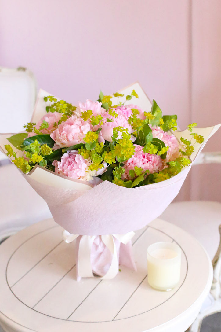 Pink peony hand-tied bouquet with pittosporum and gardenia leaves wrapped in fine paper