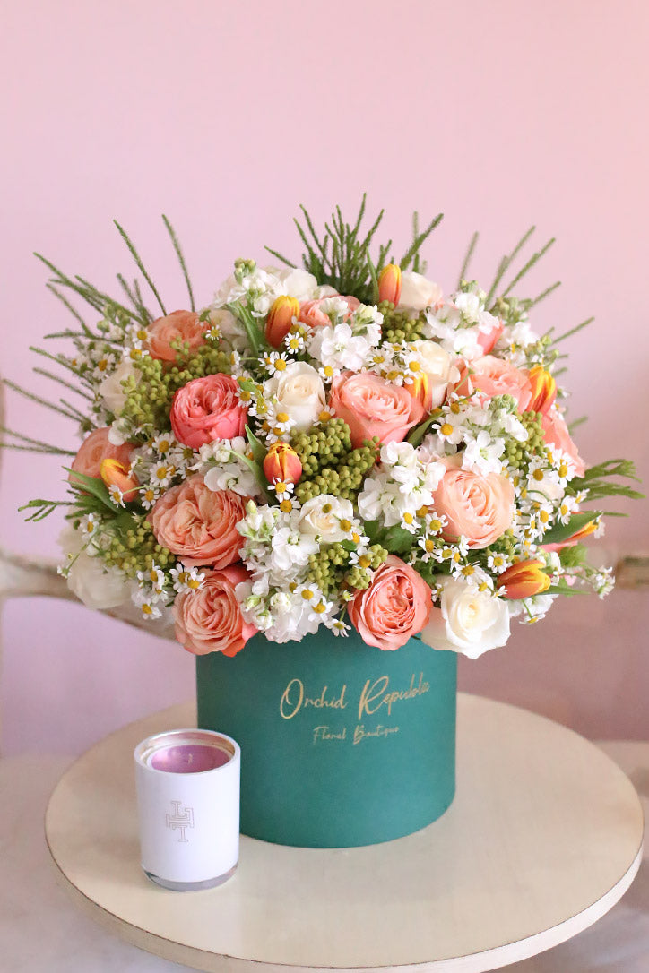 Orange tulips with salmon pink and cream garden roses, white stock, and daisies in a classic teal hatbox.