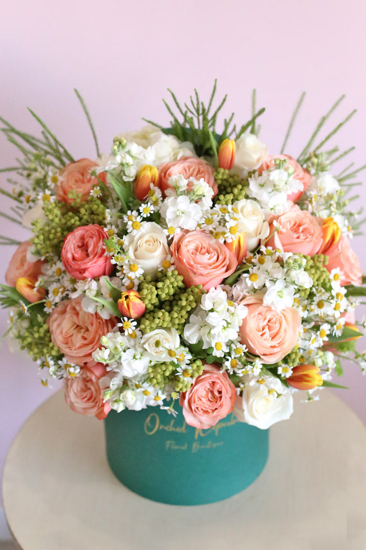 Overhead view of orange tulips, salmon pink and cream garden roses, framed by white stock and delicate daisies