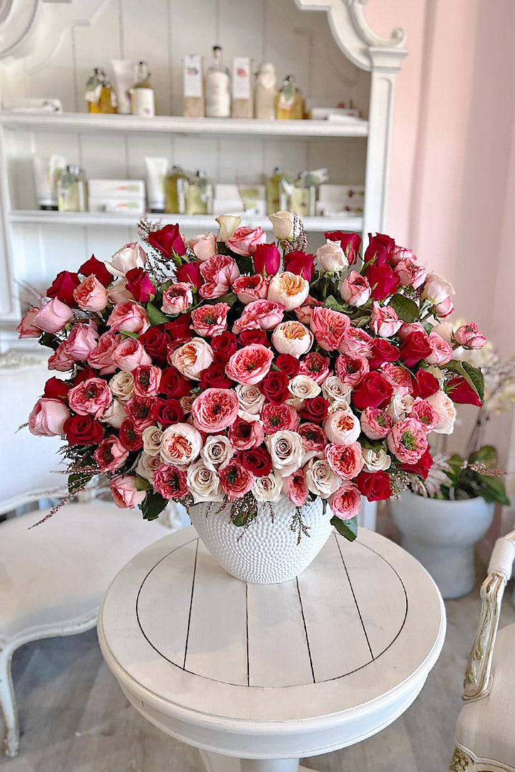 Quicksand, red and Mandarin Expression roses arranged in a grand white vase