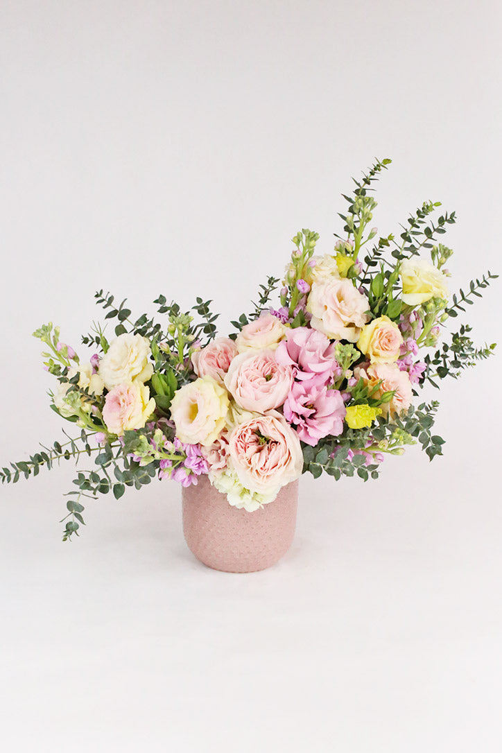 Pastel garden roses, spray roses, lisianthus and stock in a pink ceramic vase