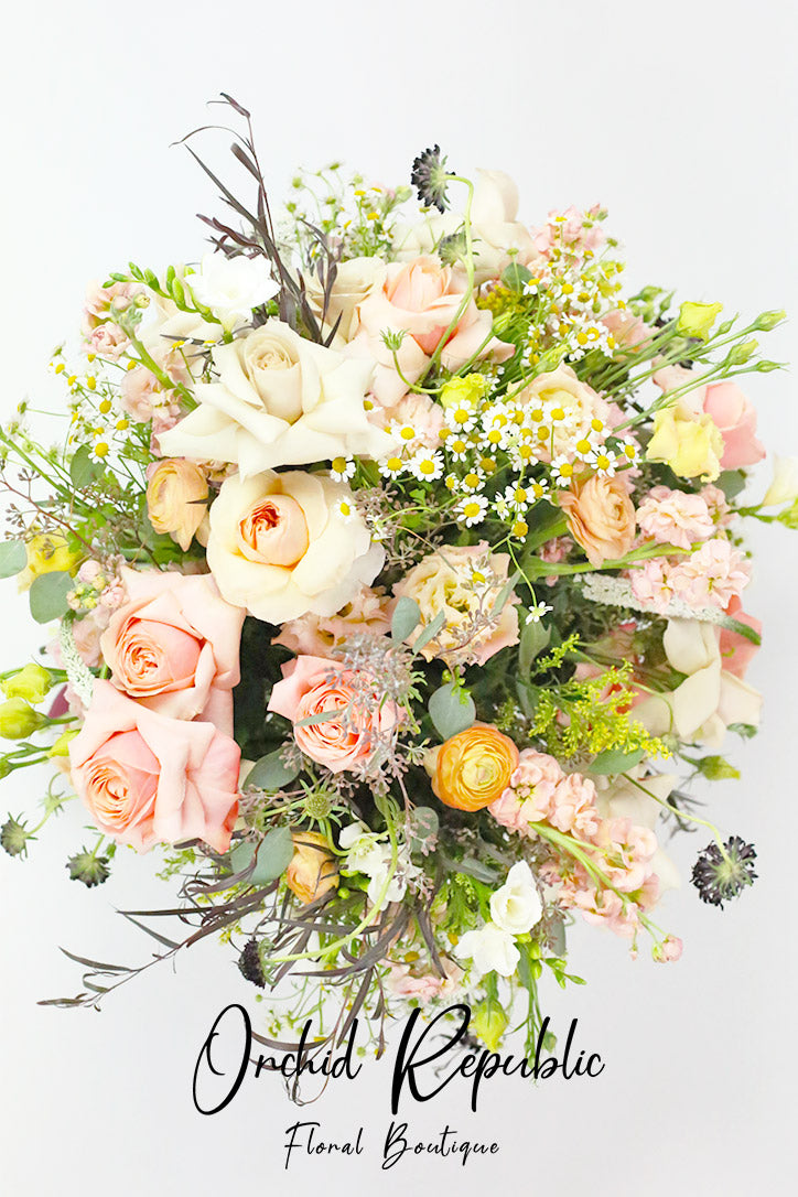 Hand-tied bouquet of soft-hued roses, yellow ranunculus, chamomile, and black scabiosa