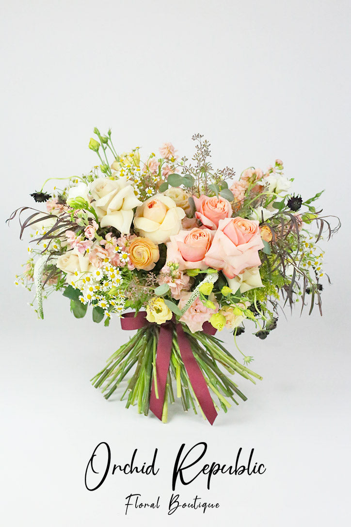 Blush and champagne rose bouquet with yellow ranunculus and chamomile tied with decorative ribbon 