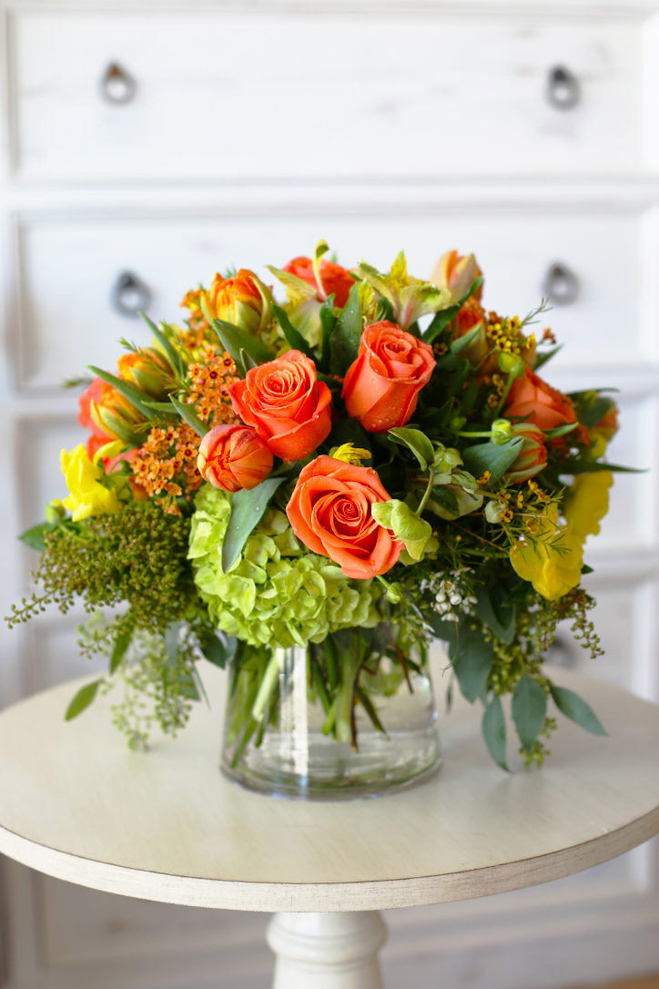 Orange roses and tulips with yellow hellebores in a cylindrical glass vase