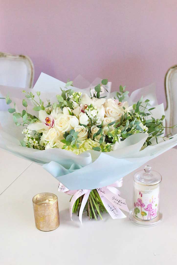 All-white bouquet of creamy white roses, tulips, hydrangeas, and white Cymbidium orchids wrapped in fine paper