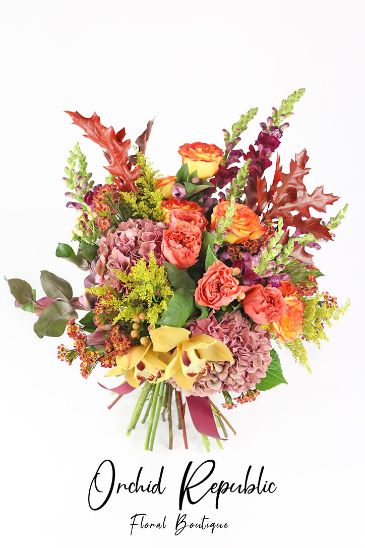 Autumn bouquet of golden cymbidium orchids, fiery orange roses, hydrangeas, and snapdragons