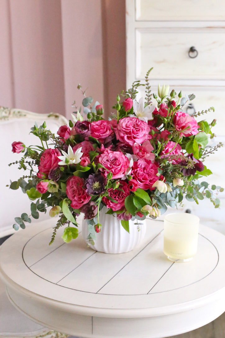 Pink Country Blue roses, butterfly ranunculus, hellebores, white clematis, and eucalyptus in a white fluted vase