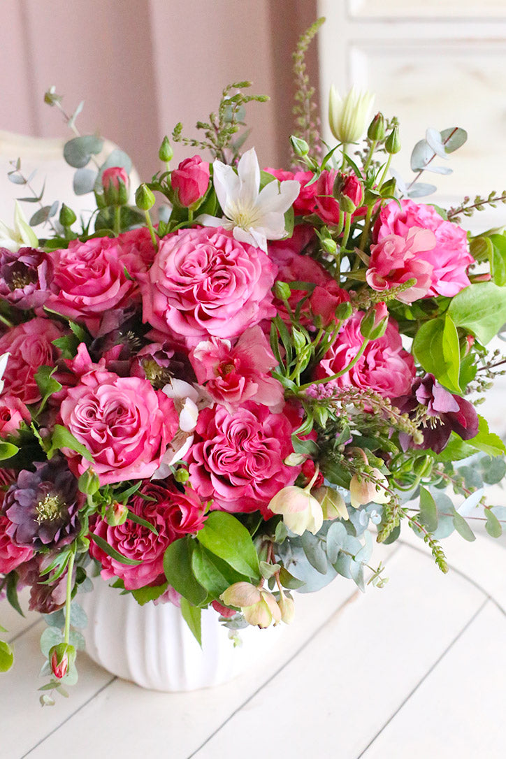 Side view of pink Country Blue roses with ranunculus, hellebores and white clematis