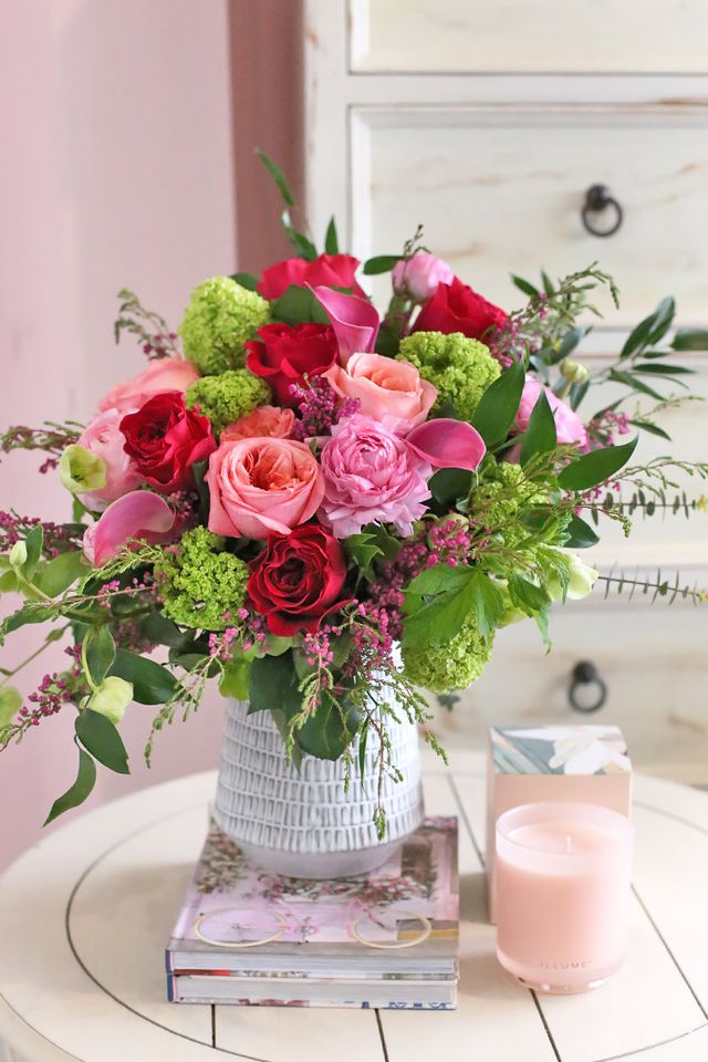 Pink, red and hot pink roses with calla lilies and hellebores in a white ceramic vase