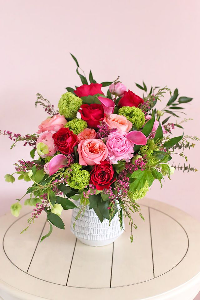 Pink, red and hot pink roses with calla lilies and hellebores in a white ceramic vase