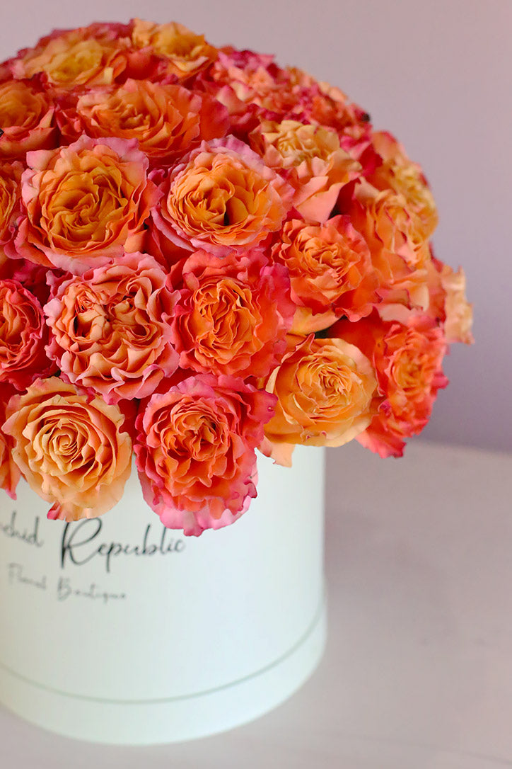 Dense layered view of lush orange rose blooms in an elegant hatbox 