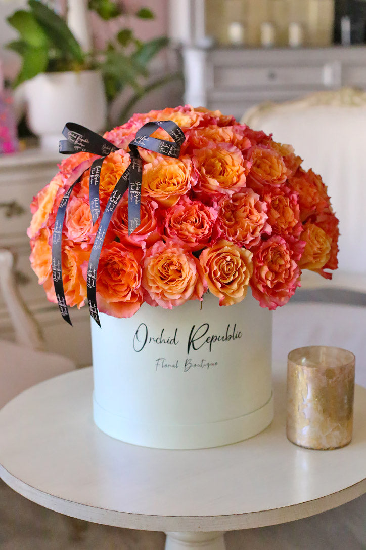 Sixty-five vivid orange roses in an elegant hat box topped with satin ribbon