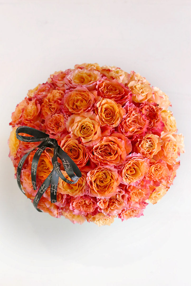 Close-up of sixty-five tightly arranged orange roses accented with a black ribbon