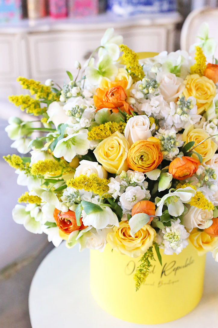 Close-up of yellow roses, goldenrod, white stock, hellebores and orange ranunculus