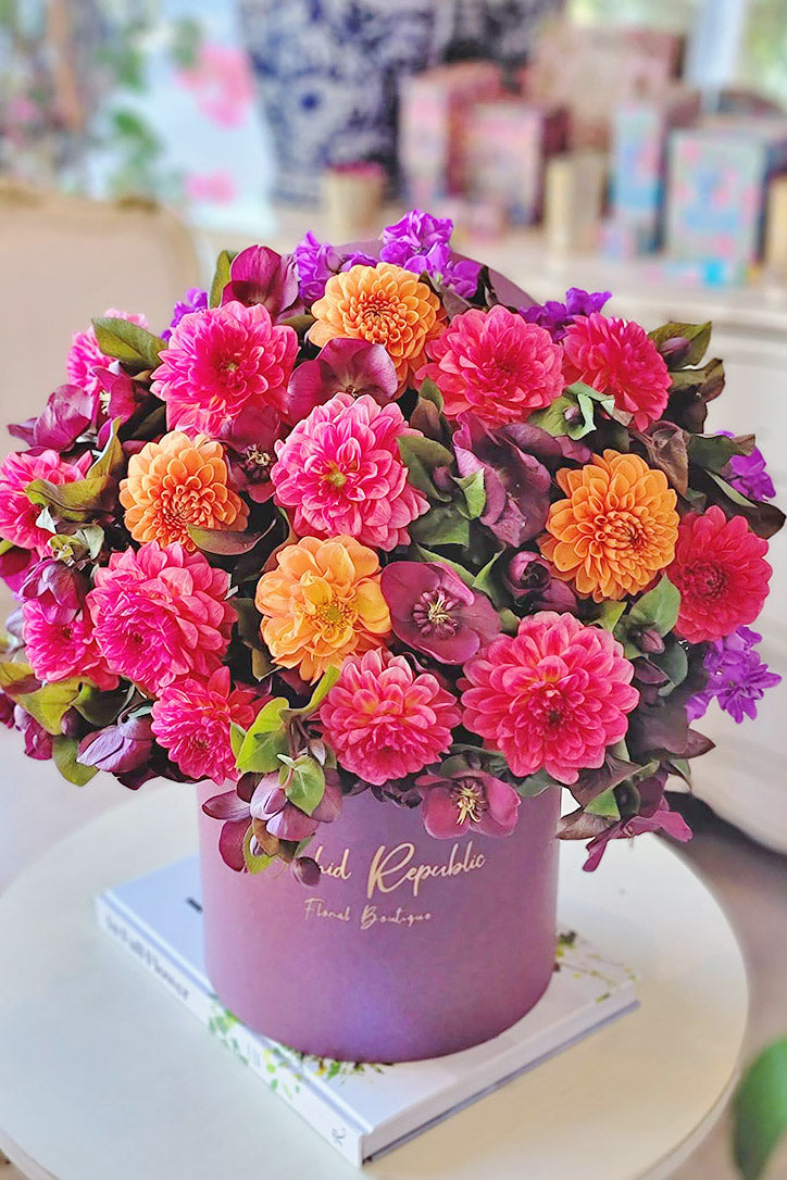 Bubblegum-pink and coral dahlias arranged with burgundy hellebores in a luxury hatbox