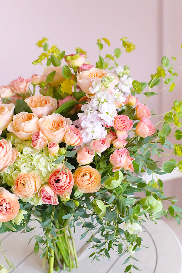 Side view of Juliet roses, ranunculus, and peach stock bouquet finished with lush greenery