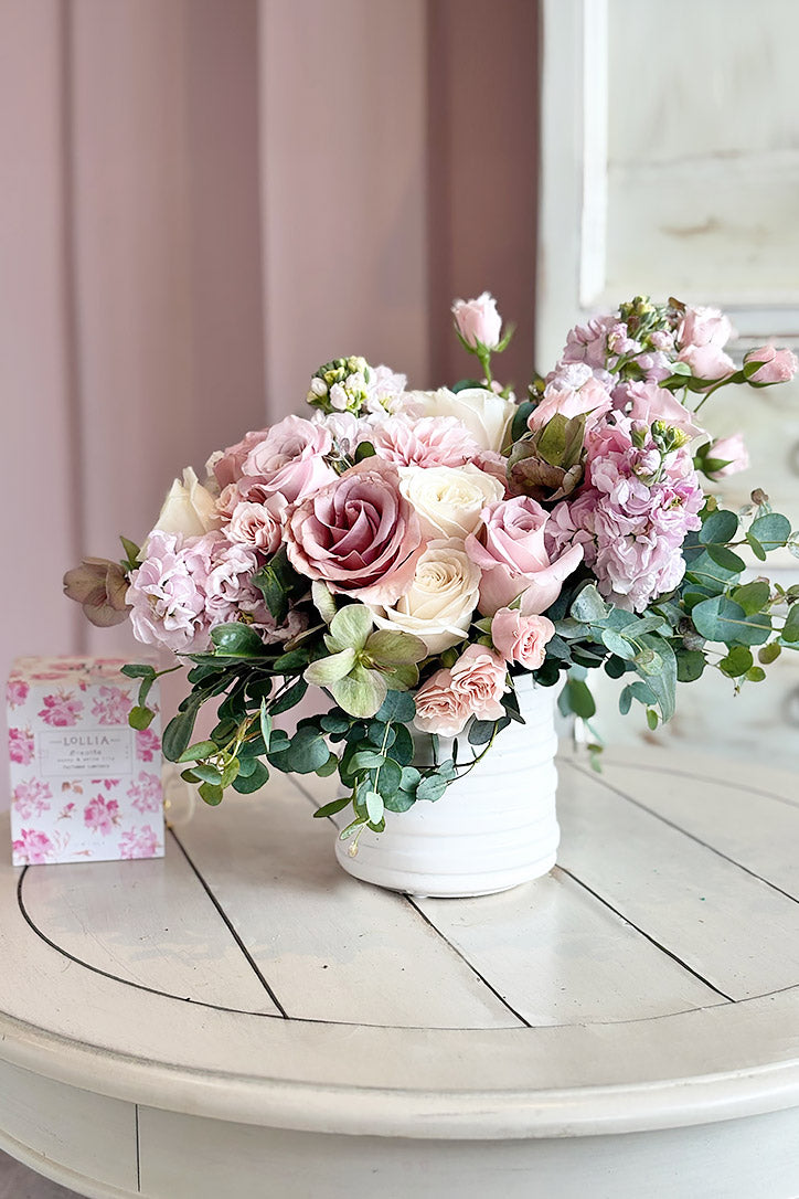Pink dahlias and roses with light pink stock and seeded eucalyptus in a stylish white vase