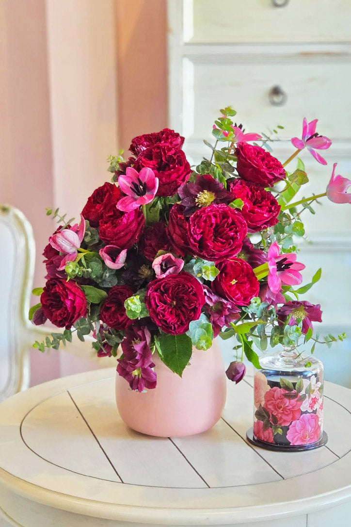 Mulberry garden roses, pink tulips and purple hellebores in a blush pink ceramic vase