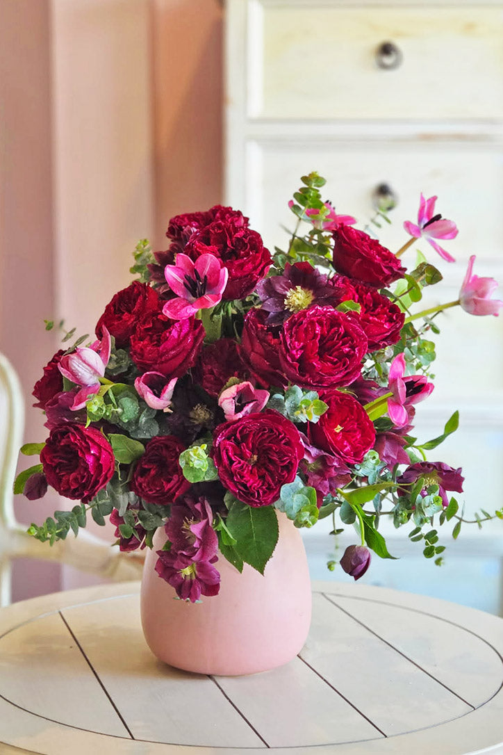 Mulberry garden roses, pink tulips and purple hellebores in a blush pink ceramic vase