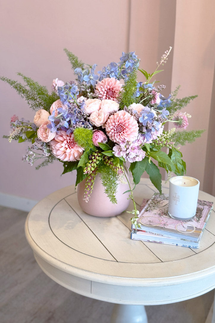 Pink dahlias, garden roses and lavender delphinium in a matte pink ceramic vase