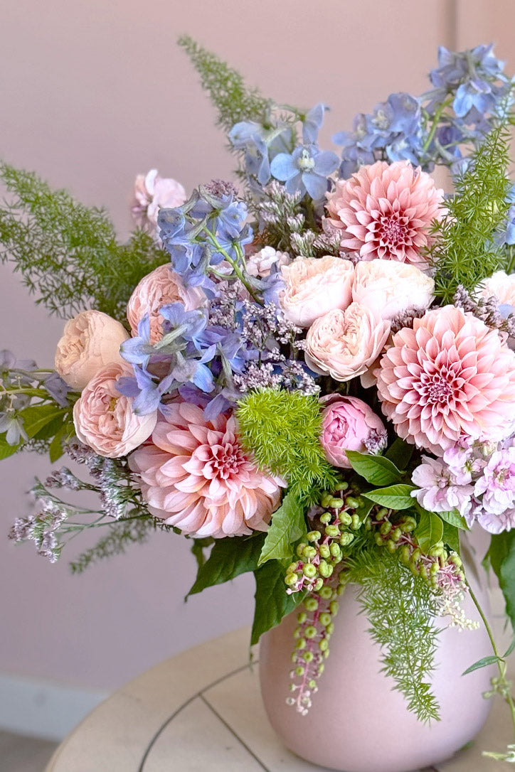 Side view of the pastel floral arrangement with fern in a matte pink ceramic vase