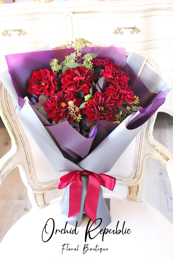 Deep wine-red dahlia hand bouquet wrapped in fine paper and finished with satin ribbon
