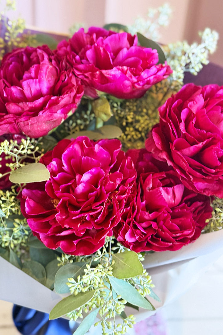Close-up of lush berry pink peonies accented with seeded eucalyptus