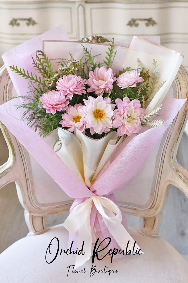 Blush pink dahlia hand bouquet with lush greenery wrapped in fine-quality paper