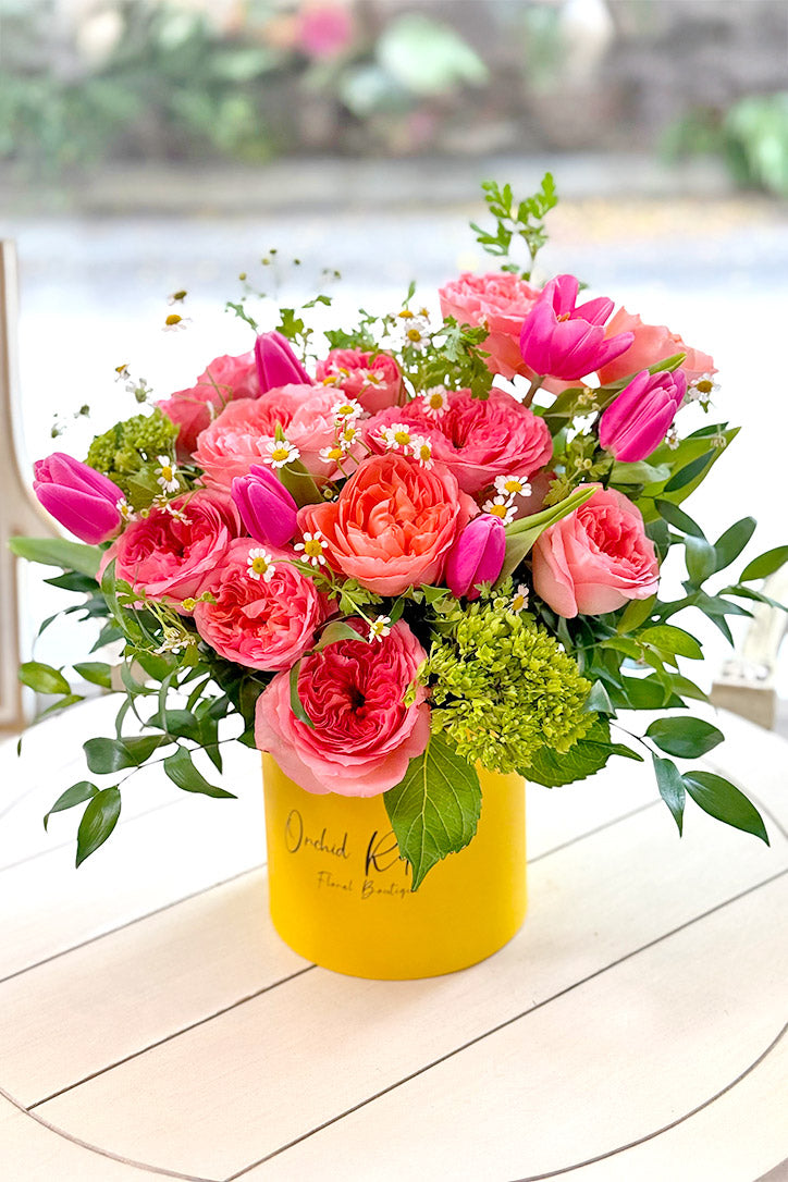 Coral roses, hot-pink tulips and green hydrangeas in a yellow hat box