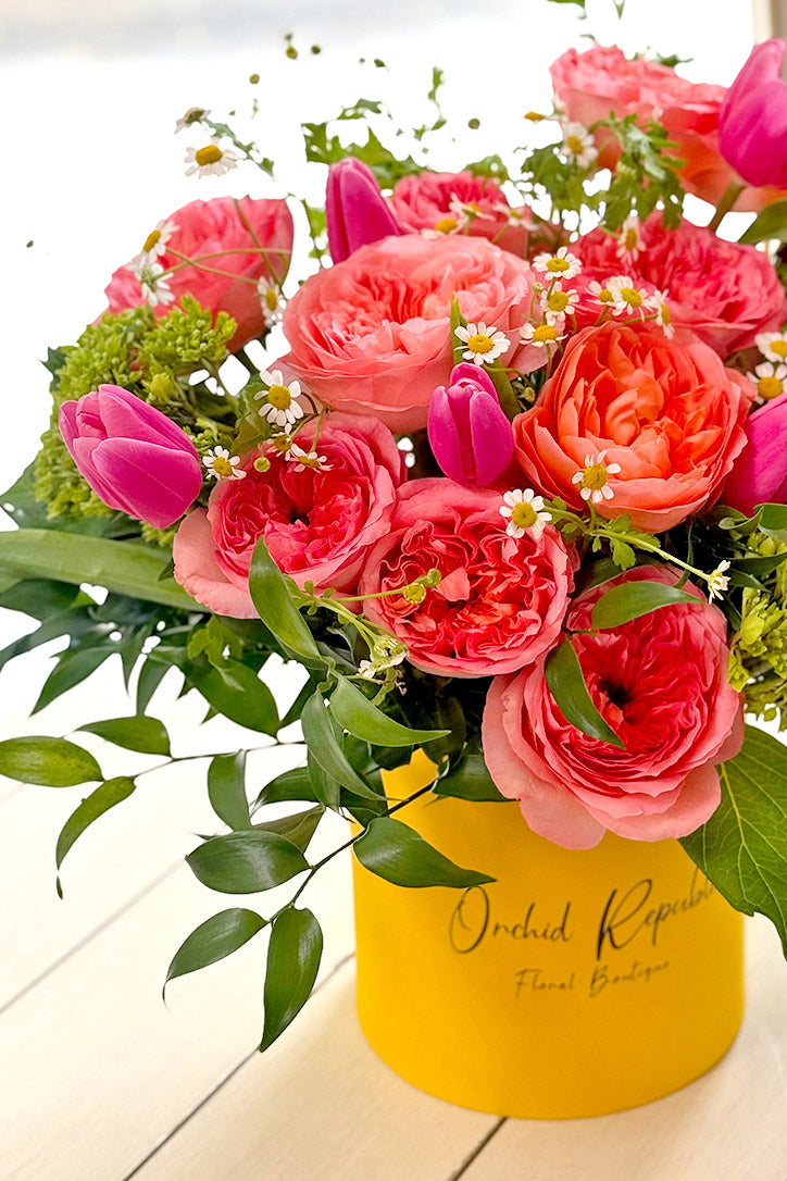 Sunny yellow hat box filled with coral, hot-pink, white and fresh green flowers