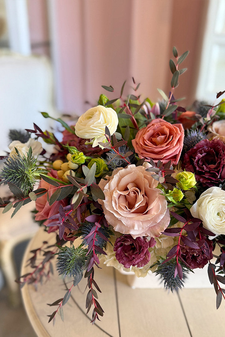 Close-up of neutral roses, white ranunculus, blue thistle and mulberry queen protea